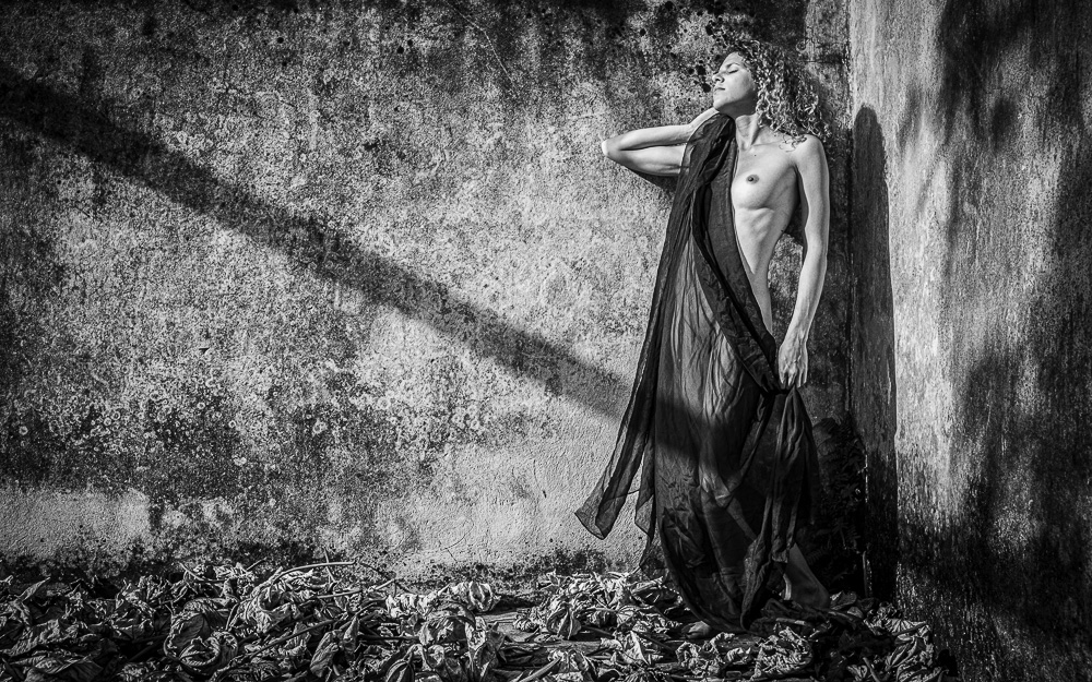 Nude model with black drapery in an abandoned beach bath house with dead leaves at her feet - Fine art nude photography workshop in Cuba - Havana